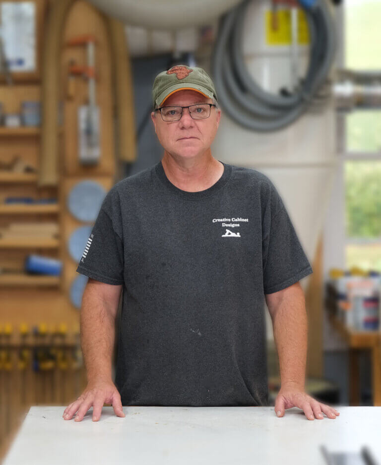 Picture of Brent Harral standing in his workshop with hands on assembly table